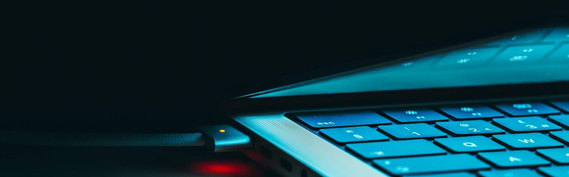 Close-up of a glowing laptop keyboard and lid in a dark setting, highlighting technology and design.